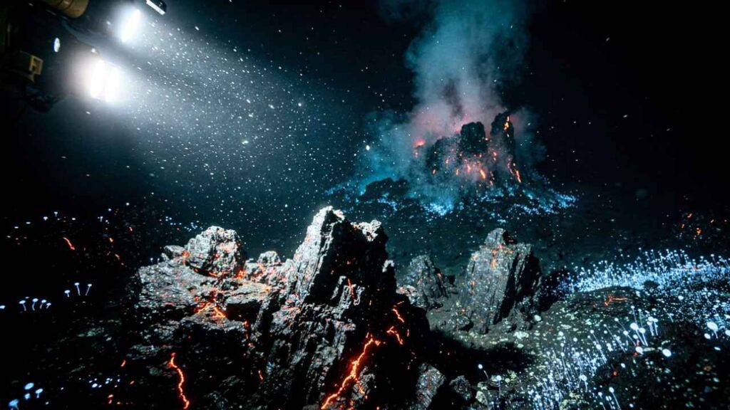 Rochas vulcânicas no fundo do Oceano Pacífico, iluminadas por submarino, com microrganismos bioluminescentes visíveis em fissuras a mais de 4.000 metros de profundidade