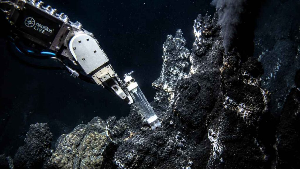 Braço robótico coleta amostras em uma fossa oceânica profunda próxima a fontes hidrotermais, onde cientistas estudam microrganismos extremos que podem ajudar na busca por vida fora da Terra.