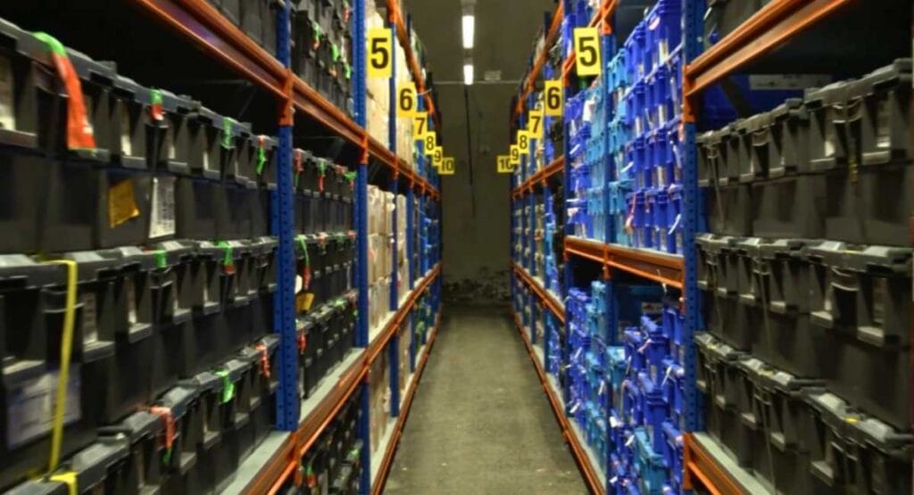 Corredor de depósito com prateleiras cheias de caixas numeradas de 5 a 10, organizadas para armazenamento.