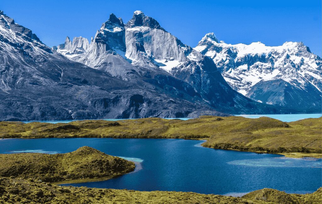 Montanhas nevadas com picos irregulares e lago azul turquesa em paisagem verde sob céu claro cordilheira dos andes maior barreira natural do mundo