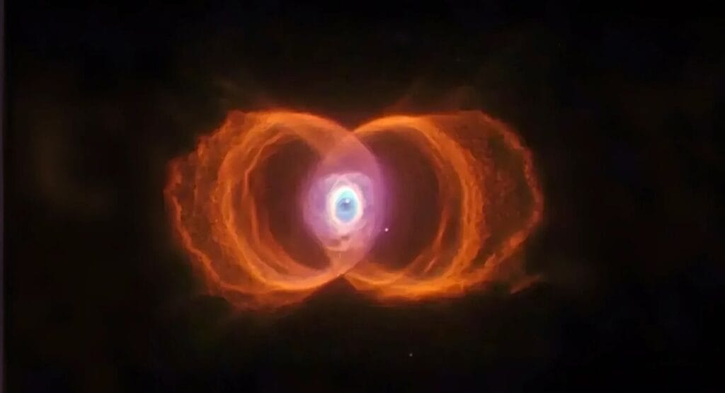 Nebulosa em forma de ampulheta com lobos laranja simétricos e centro azul roxo brilhante no espaço negro. NASA capta imagem de nebulosa a 8 mil anos-luz que parece um anjo flutuando no espaço
