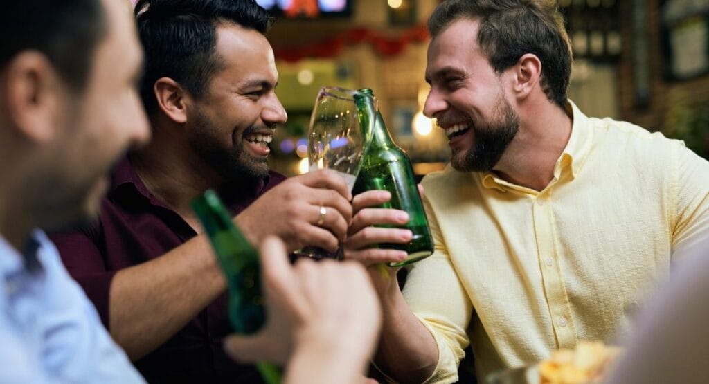 grupo de amigos em um ambiente descontraído brindando com garrafas de cerveja verdes sorrindo e interagindo alegremente. Homens que bebem podem transmitir problemas genéticos ao bebê, diz estudo
