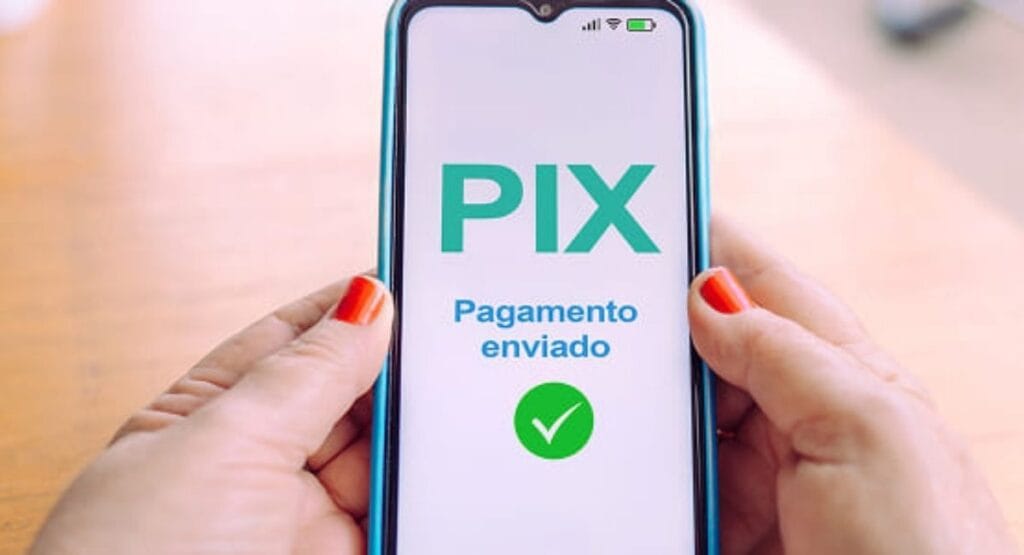 mãos segurando celular com tela exibindo PIX Pagamento enviado e marca de verificação verde, indicando transação concluída, sobre fundo claro.