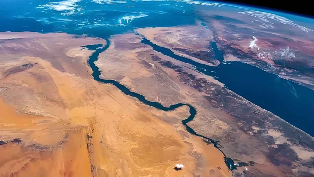 O rio Nilo é o segundo rio mais extenso do mundo.
Nenhuma imagem de satélite captura a relação simbiótica entre uma civilização e um recurso natural de forma tão dramática quanto a foto do Rio Nilo vista do espaço. Observatórios como a NASA e a Agência Espacial Europeia (ESA) fornecem registros visuais que destacam o rio em um contraste impressionante: uma faixa vibrante de verde, serpenteando através da vastidão árida e marrom do Deserto do Saara. Essa visão aérea, que remete a um "cinto verde" de vida, é a prova gráfica de que, sem o Nilo, o Egito seria quase inteiramente inabitável.Com aproximadamente 6.650 quilômetros, o Nilo é o rio mais longo do mundo, e a sua importância é indiscutível. As imagens de alta resolução revelam onde o deserto implacável cede lugar à agricultura, à infraestrutura e, crucialmente, à concentração humana, explicando por que a margem do rio se tornou o berço de uma das civilizações mais duradouras da história.O Berço da Civilização: A Terra Que a Água Criou
A história egípcia é inseparável do ciclo hidrológico do Nilo. Durante milênios, a cheia anual do rio, alimentada pelas chuvas nas terras altas da Etiópia, depositava uma camada rica e escura de sedimento nas suas margens, transformando o solo em um kemet (terra negra) incrivelmente fértil. Esse fenômeno, visível nas fotos espaciais como a área de maior densidade verde, foi o motor da revolução agrícola egípcia.Estudos históricos e arqueológicos da Organização Egípcia de Antiguidades confirmam que a previsibilidade da cheia permitiu o desenvolvimento de um calendário e de um sistema de irrigação sofisticado. A necessidade de organizar a irrigação e a distribuição da água uniu as comunidades, criando uma estrutura social complexa. Essa organização, baseada na gestão de recursos hídricos, foi a fundação para o surgimento do estado faraônico.A Importância Agrícola e Demográfica: Uma Dependência Extrema
A dependência do Nilo não é apenas histórica, mas uma realidade demográfica contemporânea. O relatório de assentamento urbano da ONU estima que mais de 95% da população egípcia vive ao longo das margens do rio ou em seu delta, uma das maiores concentrações populacionais lineares do mundo. O mapa de calor gerado a partir de dados de satélite da NASA sobre a atividade noturna do Egito simplesmente segue o trajeto do rio.A agricultura, apesar da modernização, ainda é essencial. O rio sustenta o cultivo de grãos, frutas e, historicamente, o algodão, fornecendo a base da segurança alimentar do país. A água do Nilo, filtrada e tratada, é também a principal fonte de água potável e industrial para todas as grandes cidades egípcias, desde Aswan até Alexandria.A Engenharia Moderna: O Controle das Águas
A visão do Nilo a partir do espaço também evidencia o impacto das grandes obras de engenharia. A construção da Barragem Alta de Aswan na década de 1960, um projeto supervisionado pelo Ministério de Recursos Hídricos e Irrigação do Egito, mudou fundamentalmente o fluxo do rio.A barragem criou o enorme Lago Nasser, visível nas imagens de satélite. Seu objetivo era controlar as cheias catastróficas e garantir um suprimento constante de água para irrigação e geração de eletricidade. Contudo, essa intervenção teve consequências ecológicas. A interrupção das cheias significou que o solo não recebe mais o sedimento rico em nutrientes, forçando os agricultores a dependerem de fertilizantes artificiais, um novo desafio para a sustentabilidade agrícola do país.Conclusão: A Linha da Vida da Humanidade
A foto do Nilo vista do espaço é mais do que uma imagem bonita; é uma lição de geografia, história e sustentabilidade. Ela revela a única linha de vida que permitiu o florescimento de uma das mais antigas e resilientes civilizações humanas. A dependência contínua do Egito em relação ao rio, tanto para a sobrevivência diária quanto para a identidade cultural, sublinha a importância crítica dos recursos hídricos. O Nilo não é apenas um rio, mas o eixo vital que moldou a humanidade.