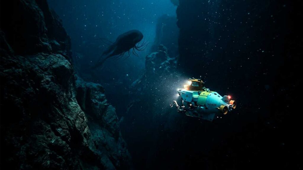 fotografia documental ultra-realística mostra o pequeno submersível de pesquisa "Alvin" descendo para o abismo escuro do fundo do oceano. O submersível branco e laranja é o único ponto de luz na cena, iluminando a água turva e cheia de partículas enquanto se aproxima de paredes de desfiladeiros subaquáticos imponentes e irregulares. À distância, uma criatura marinha misteriosa e sombria paira na escuridão.